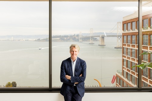 Allan Thygesen står foran et stort vindue med en bro og bygning bag sig