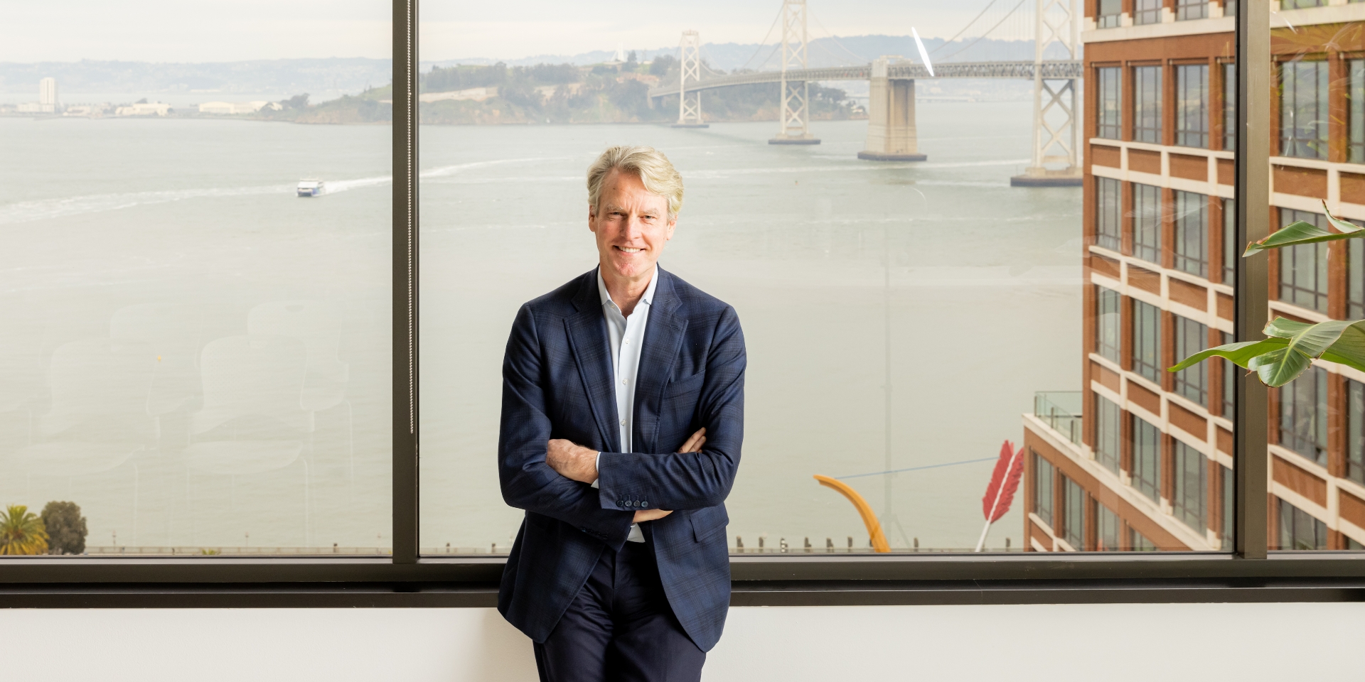 Allan Thygesen står foran et stort vindue med en bro og bygning bag sig