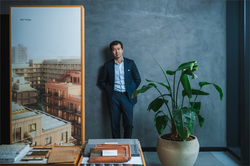 Dariush Rezai står ved siden af en grøn plante og et billede af nogle bygninger