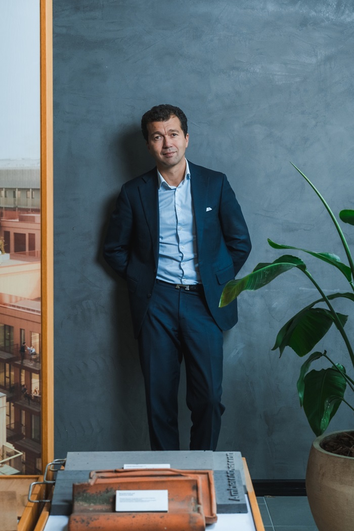 Dariush Rezai står ved siden af en grøn plante og et billede af nogle bygninger