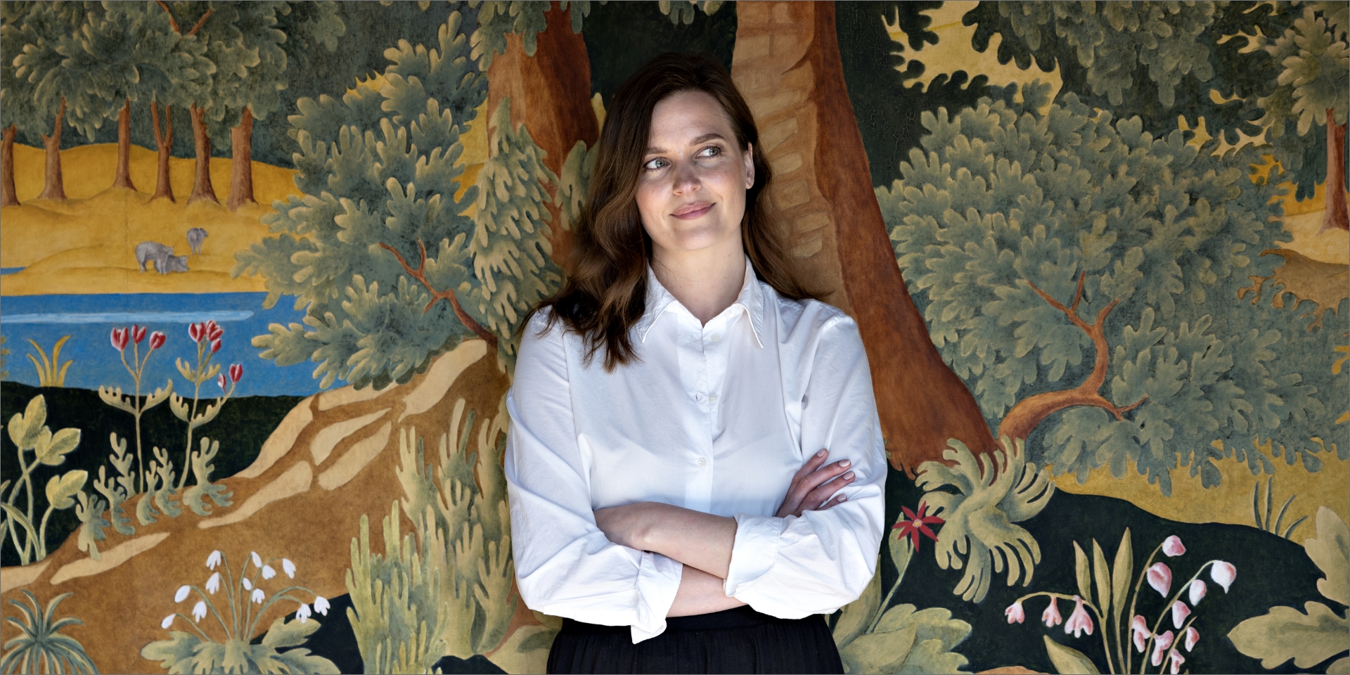 Julie Rokkjær Birch står foran et maleri med armene over kors