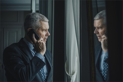 Kim Kristensen står og snakker i telefon og kigger ind i et vindue, der reflekterer hans spejlbillede