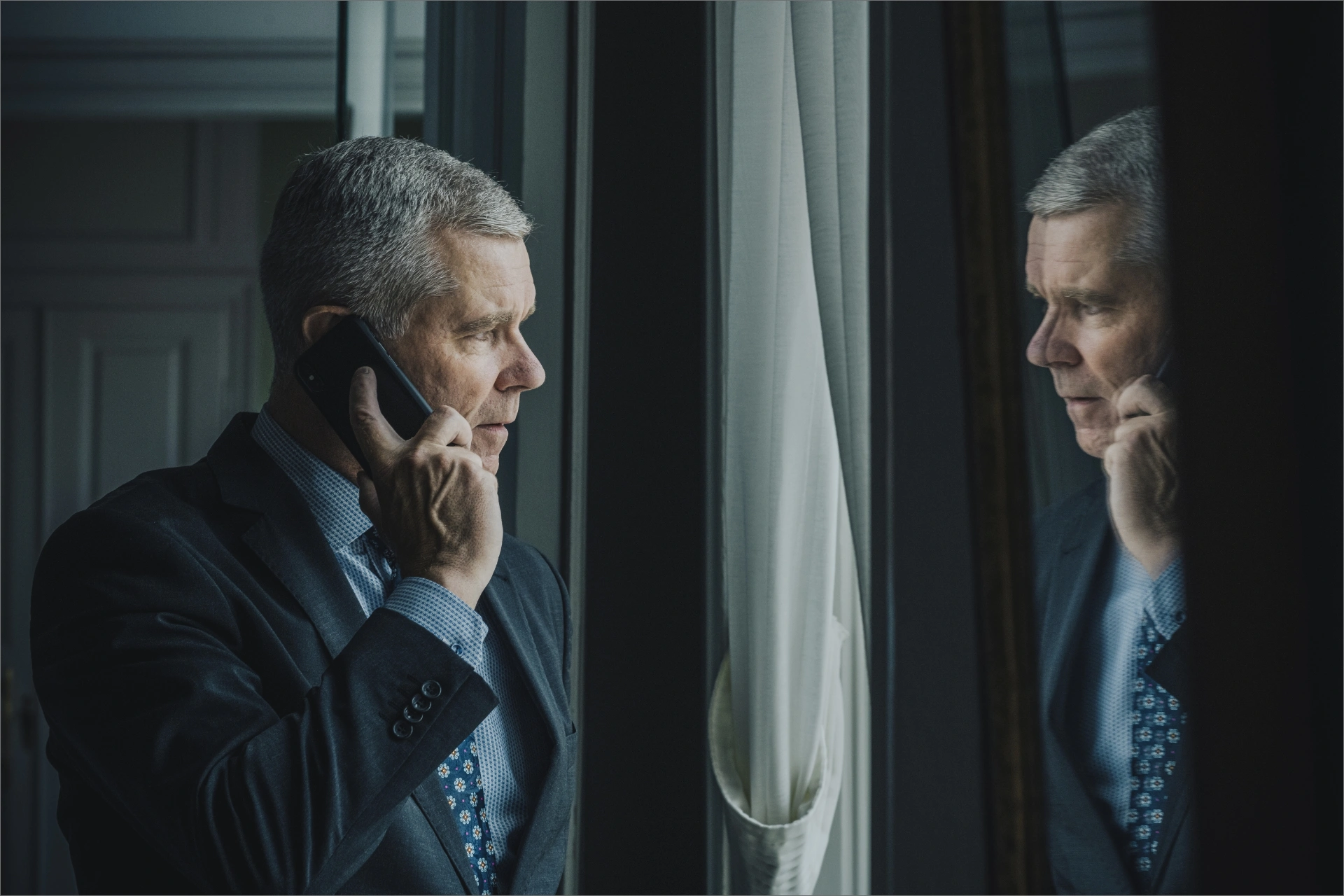 Kim Kristensen står og snakker i telefon og kigger ind i et vindue, der reflekterer hans spejlbillede