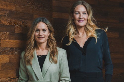 Louise Dinesen og Vibeke Lunding-Gregersen står ved siden af hinanden foran en trævæg