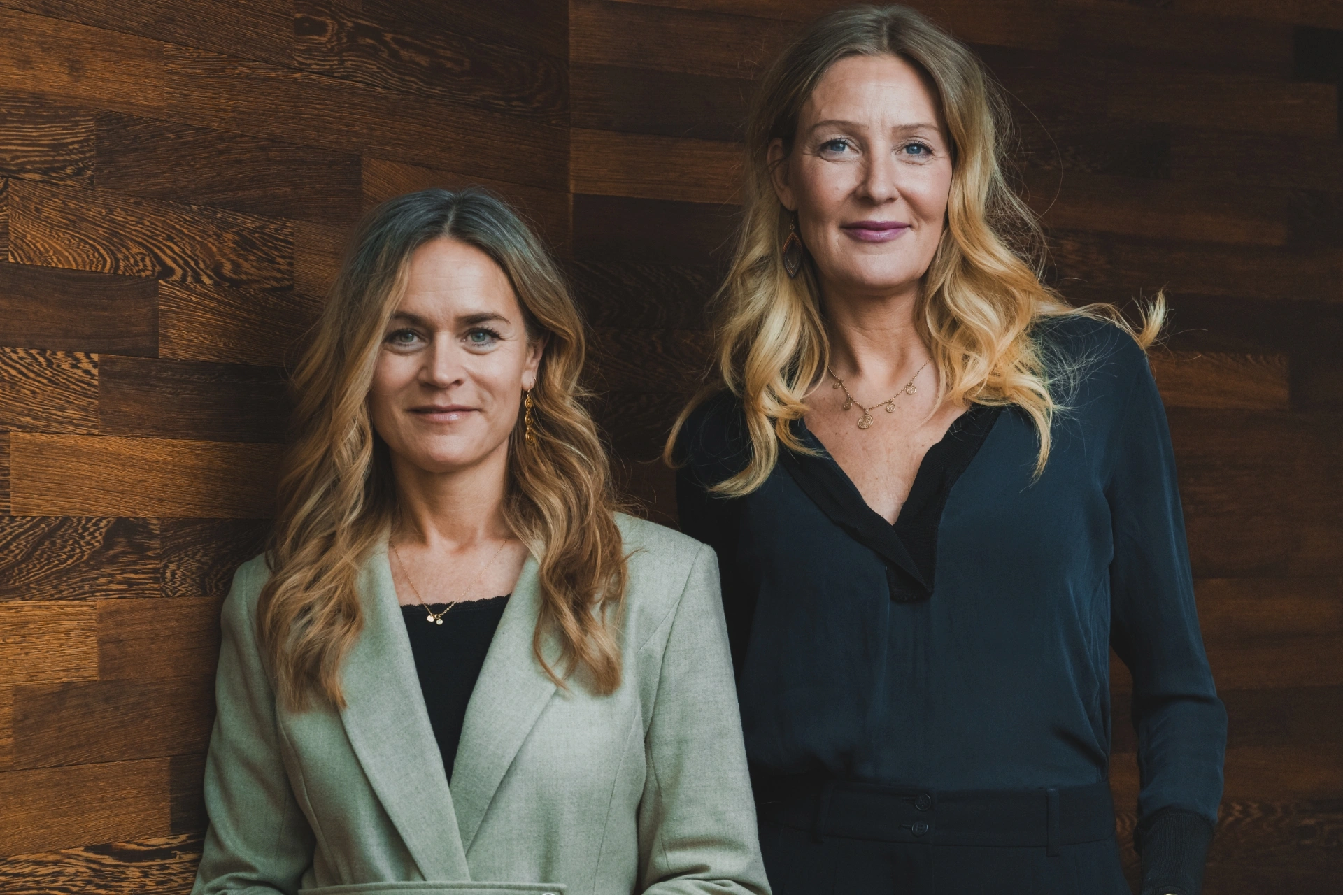 Louise Dinesen og Vibeke Lunding-Gregersen står ved siden af hinanden foran en trævæg