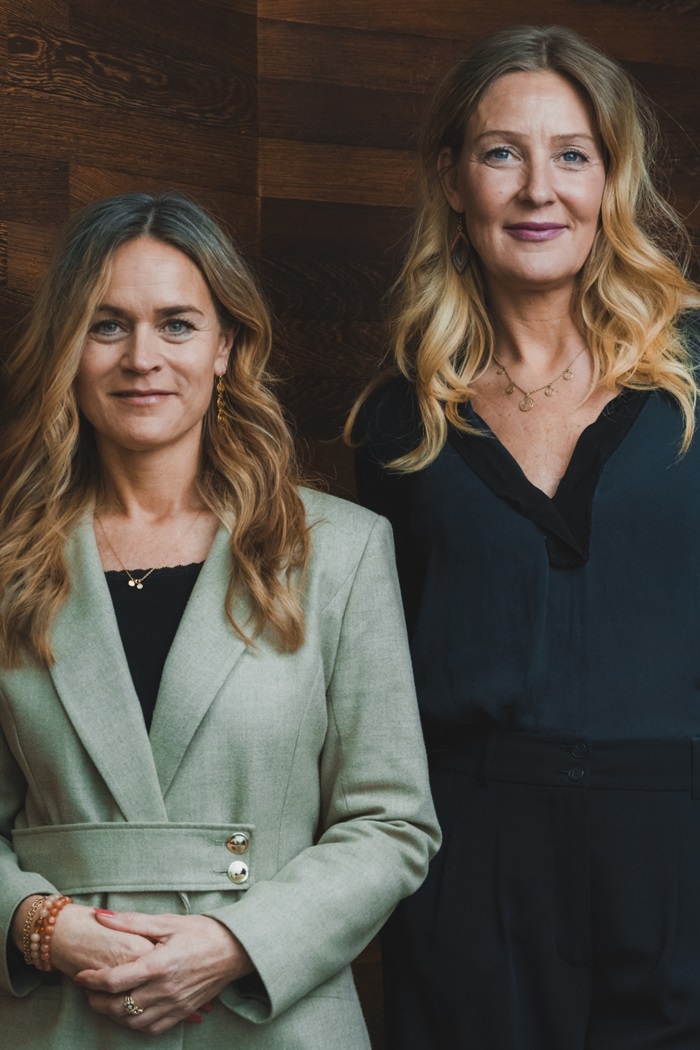 Louise Dinesen og Vibeke Lunding-Gregersen står ved siden af hinanden foran en trævæg