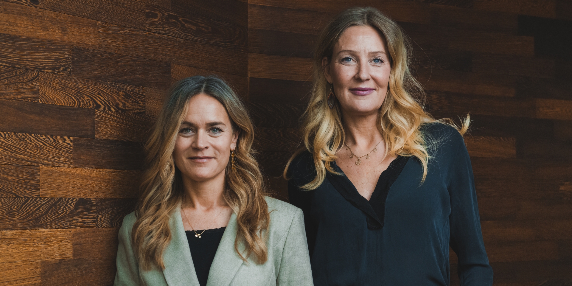 Louise Dinesen og Vibeke Lunding-Gregersen står ved siden af hinanden foran en trævæg
