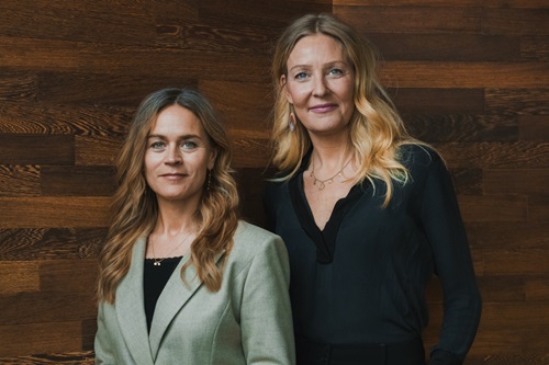 Louise Dinesen og Vibeke Lunding-Gregersen står ved siden af hinanden foran en trævæg