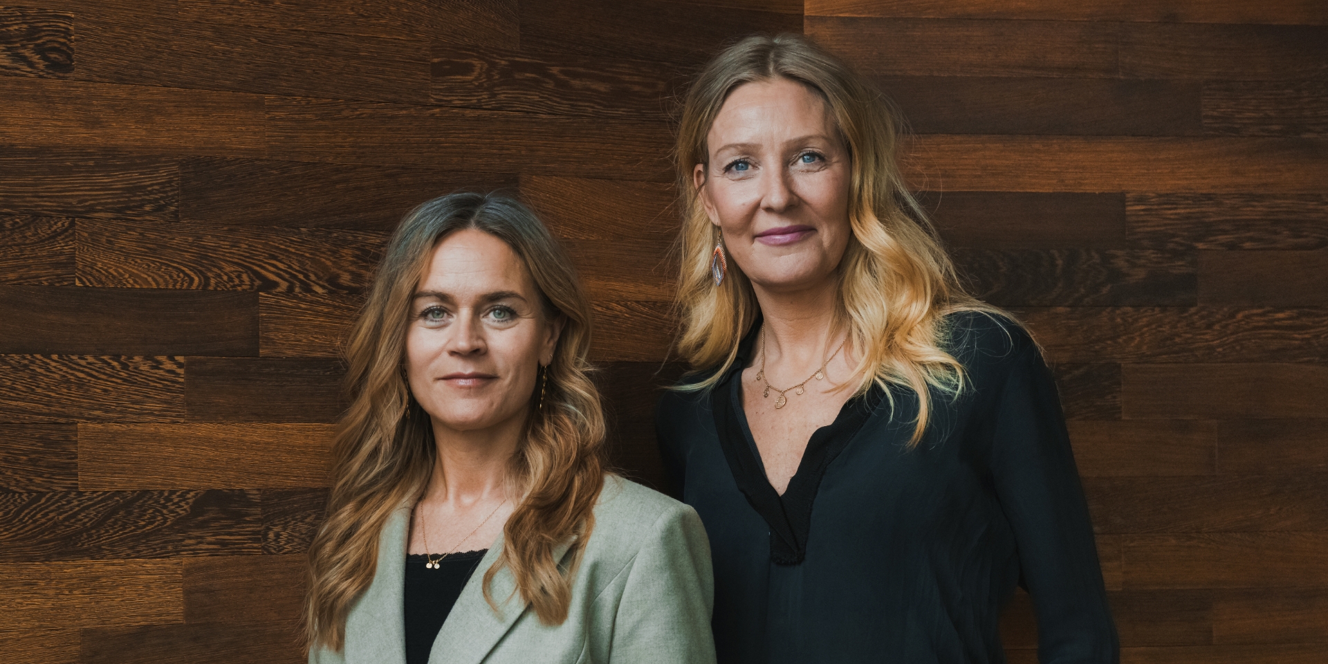 Louise Dinesen og Vibeke Lunding-Gregersen står ved siden af hinanden foran en trævæg