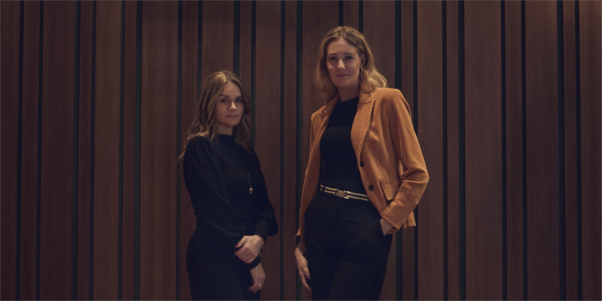 Vibeke Lunding Gregersen og Louise Dinesen står ved siden af hinanden foran træpanel