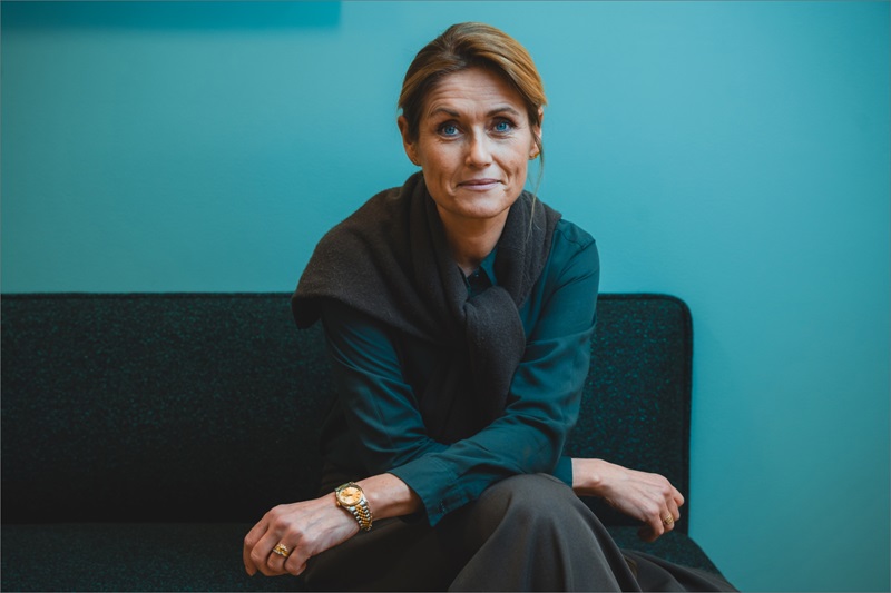 Nina Kovsted Helk sidder i en sofa med turkis baggrund