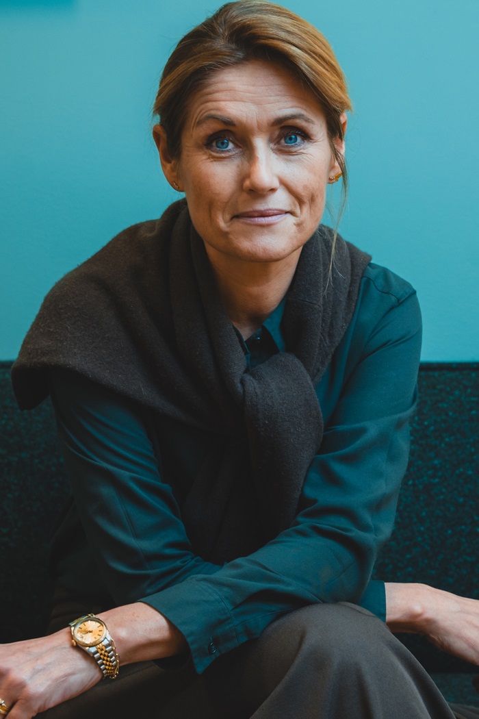 Nina Kovsted Helk sidder i en sofa med turkis baggrund