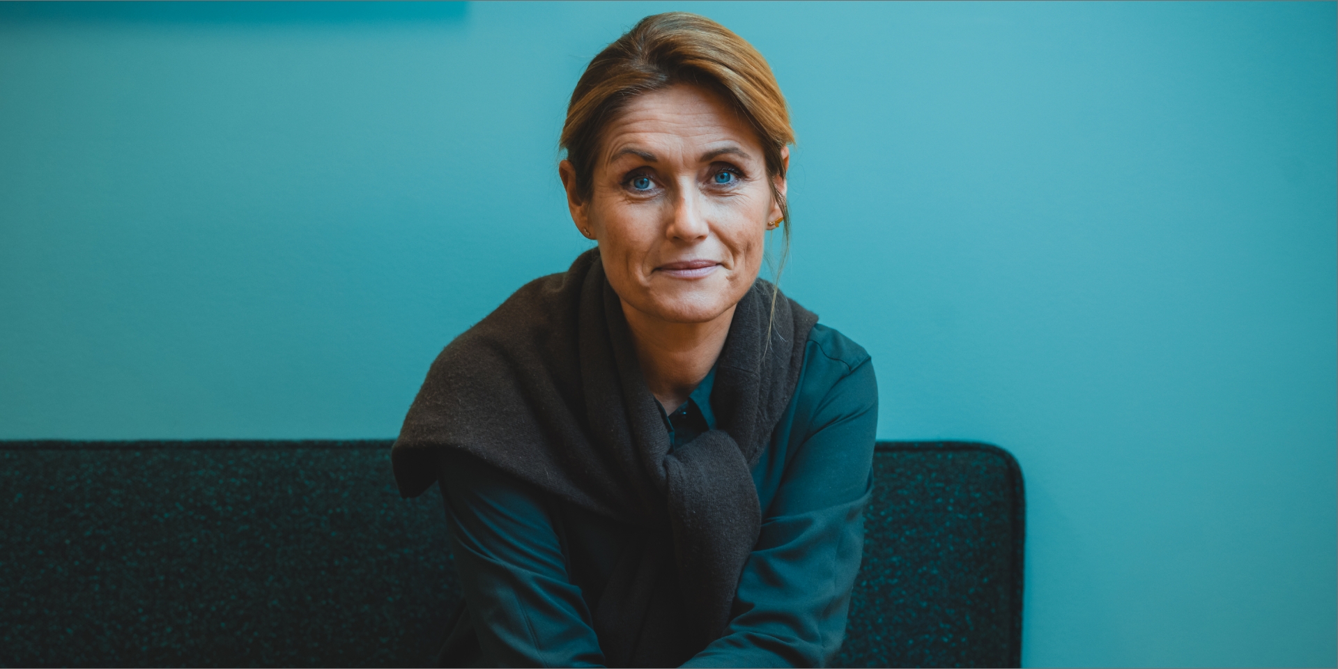 Nina Kovsted Helk sidder i en sofa med turkis baggrund