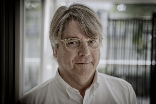 Peter Lund Madsen står i hvid skjorte og smiler