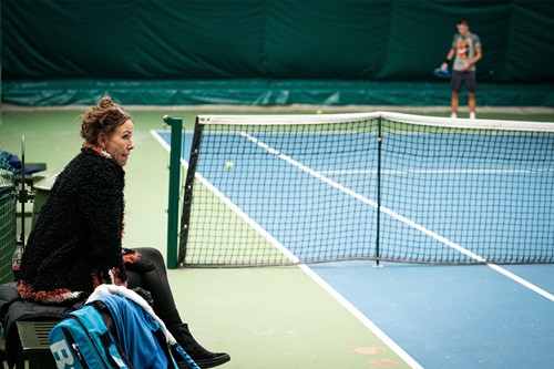 Aneke Rune ved en tennisbane mens sønnen spiller