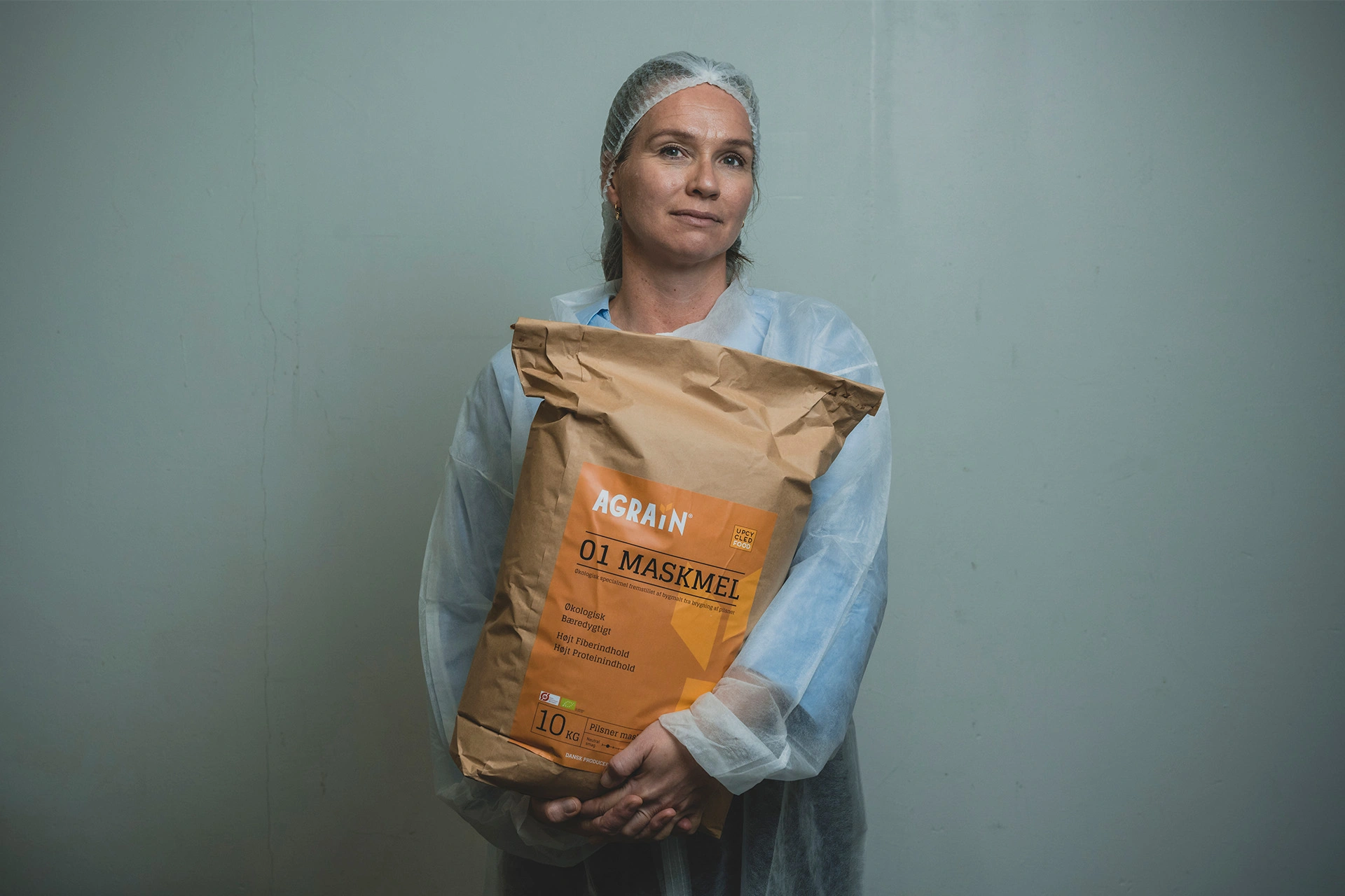 Aviaja Andersen står med en sæk maskmel iført hår net