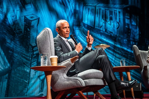 Barack Obama sidder i en grå, dansk design lænestol med en løftet pegefinger