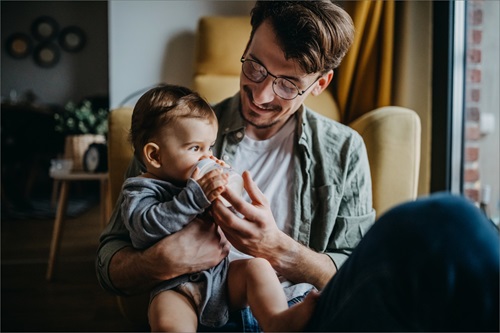 En mand sidder med sit barn på skødet og giver flaske