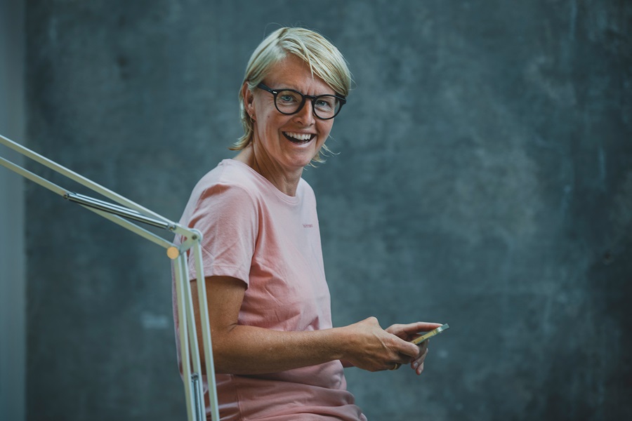 Camilla Andersen læner sig op af et bord og griner med en telefon i hånden