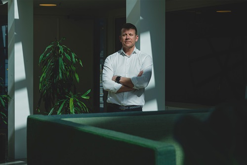 Christian Lauritzen står ved en sofa og en plante