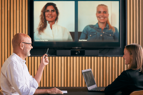 En mand og en kvinde sidder i et rum med et virtuelt møde med to kvinder