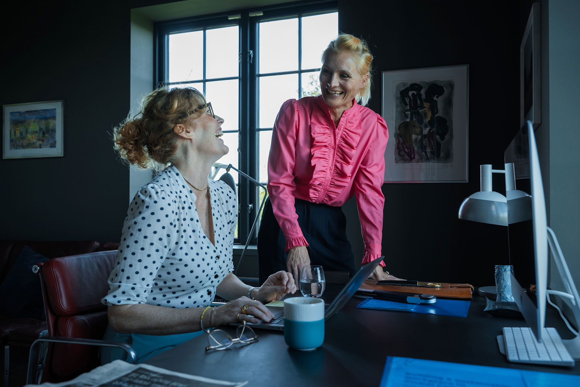 Pia Hauge og Katrine Sperling griner ved et skrivebord