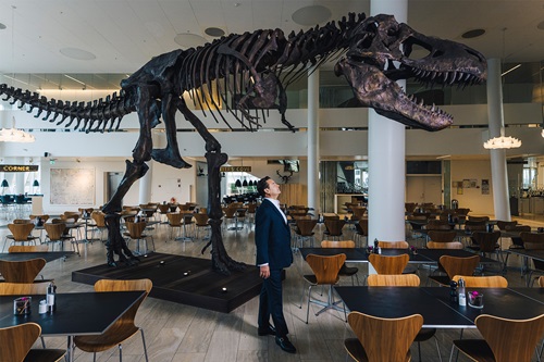 Kim Fournais står på Saxo Banks kontor med et T-Rex skelet 