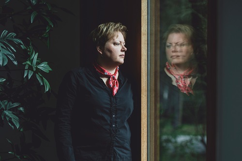 Nina Jørgensen står og ser ud af et vindue hvori man kan se hendes refleksion