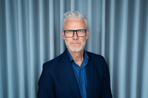 Palle Knudsen står foran en blå baggrund