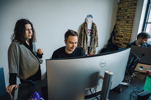 Sophie Bohr Grønbæk står og snakker med ung medarbejder ved skrivebord