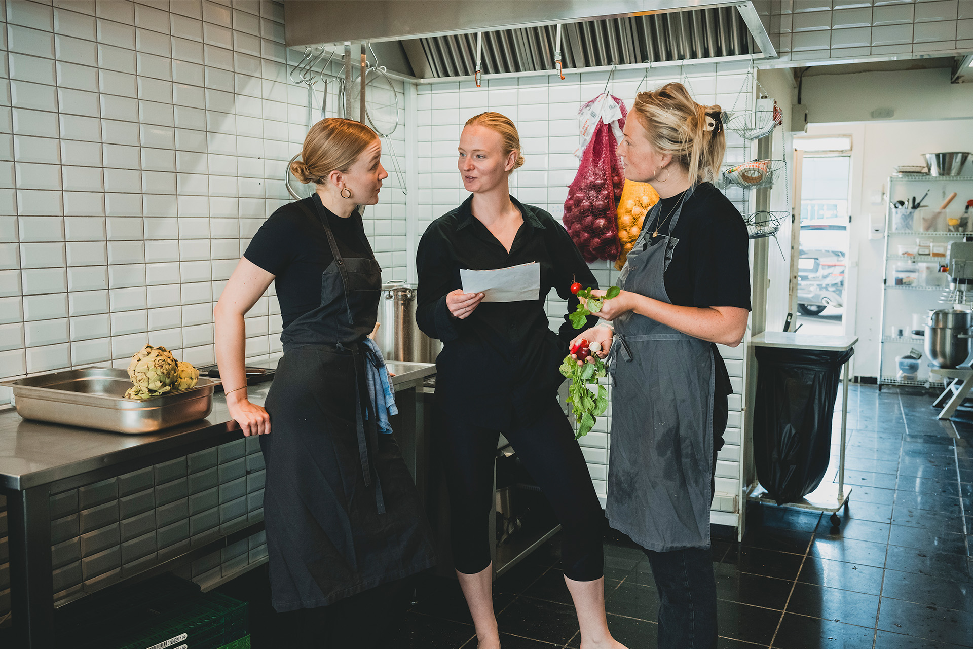 Stine Kirkegaard står i et køkken med to kolleager og snakker om menu
