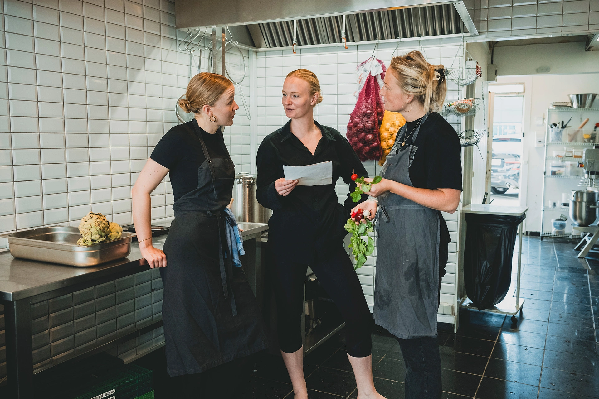Stine Kirkegaard står i et køkken med to kolleager og snakker om menu