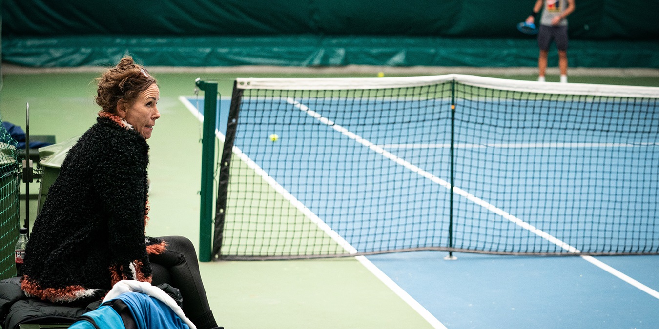 Aneke Rune ved en tennisbane mens sønnen spiller