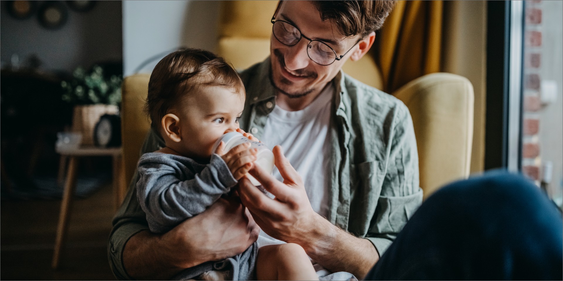 En mand sidder med sit barn på skødet og giver flaske