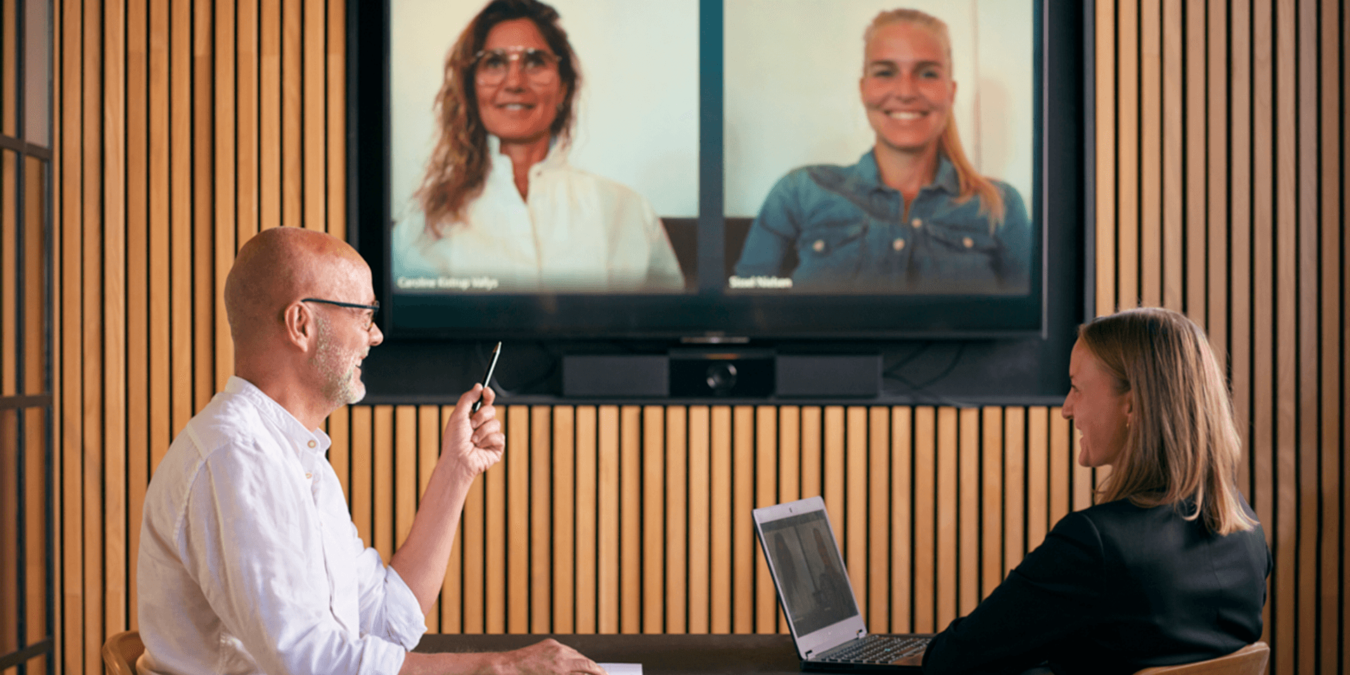 En mand og en kvinde sidder i et rum med et virtuelt møde med to kvinder