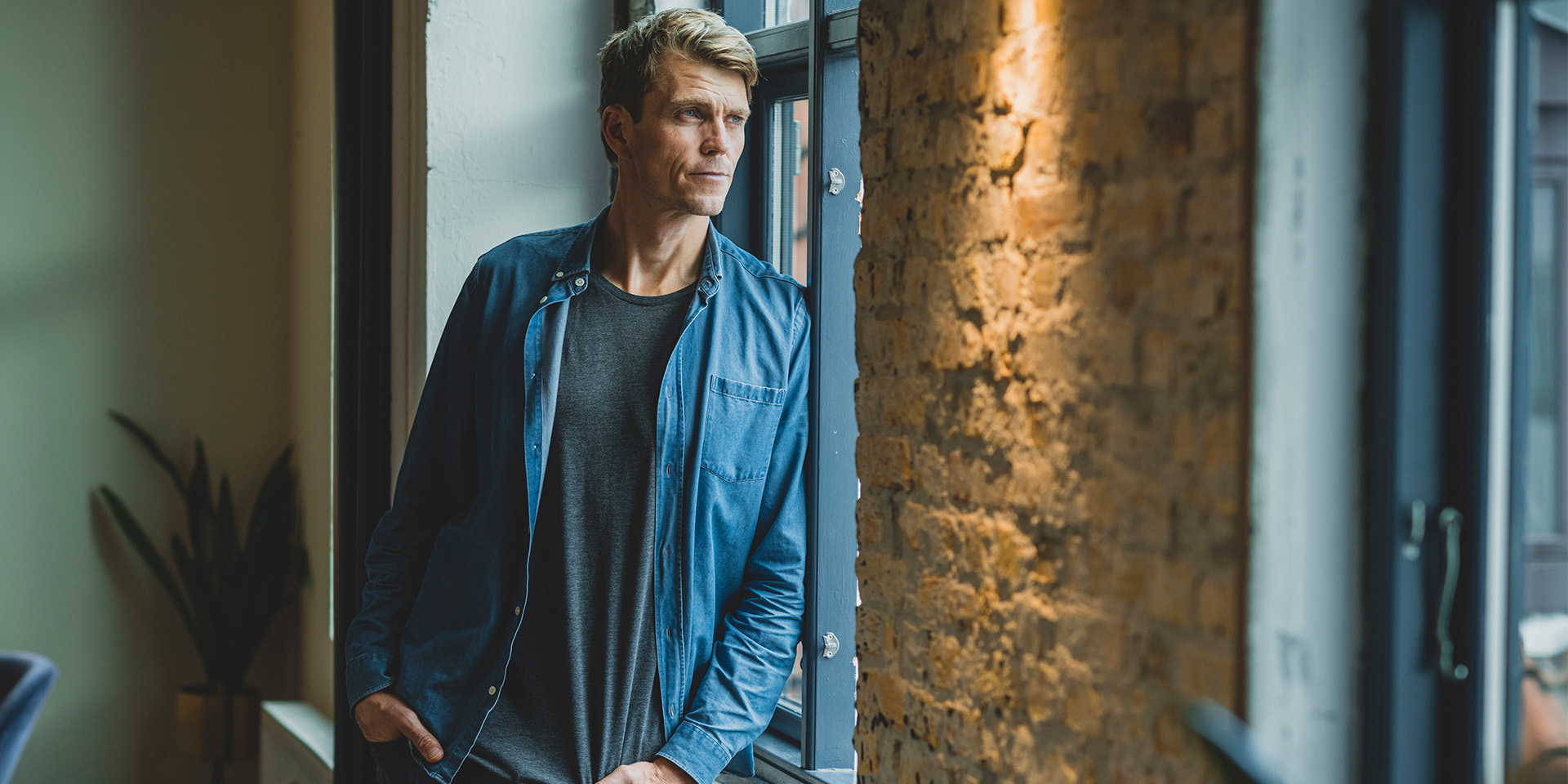 Nomineret til Årets Leder 2022, Jeppe Rindom kigger ud af et vindue mens han læner sig op af væggen