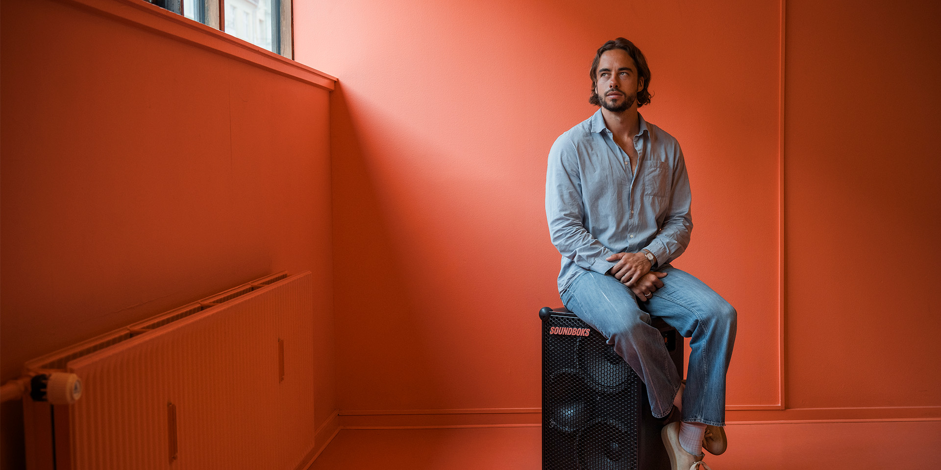 Jesper Thiel Thomsen sidder på en soundboks i et rødt lokale