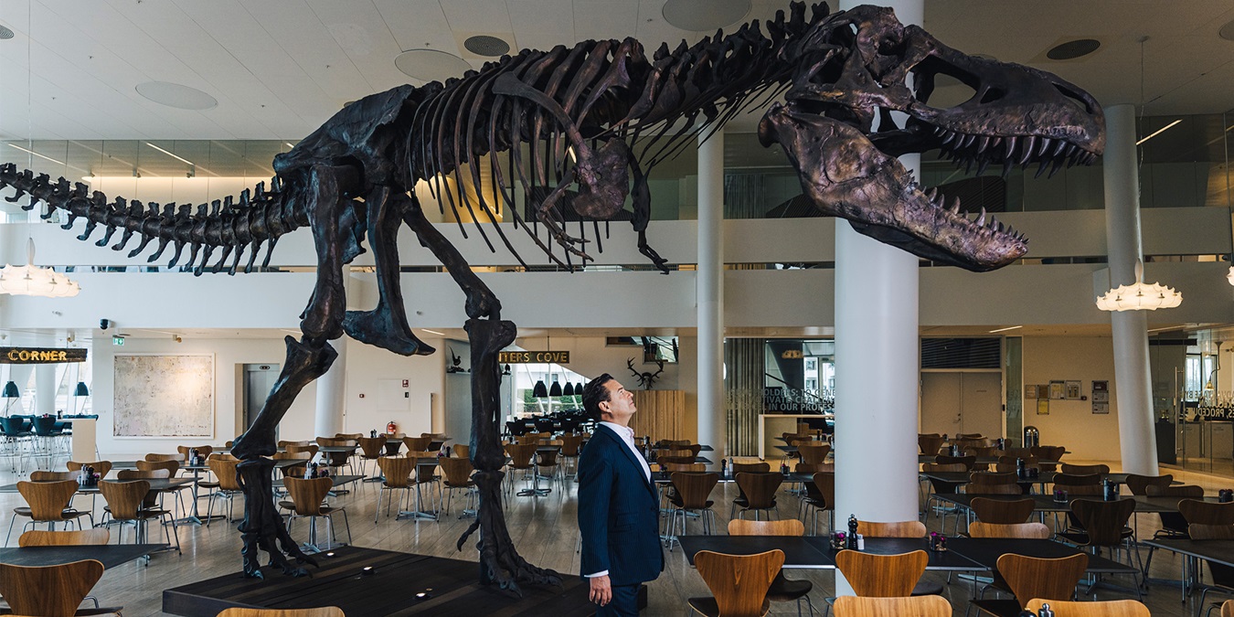 Kim Fournais står på Saxo Banks kontor med et T-Rex skelet