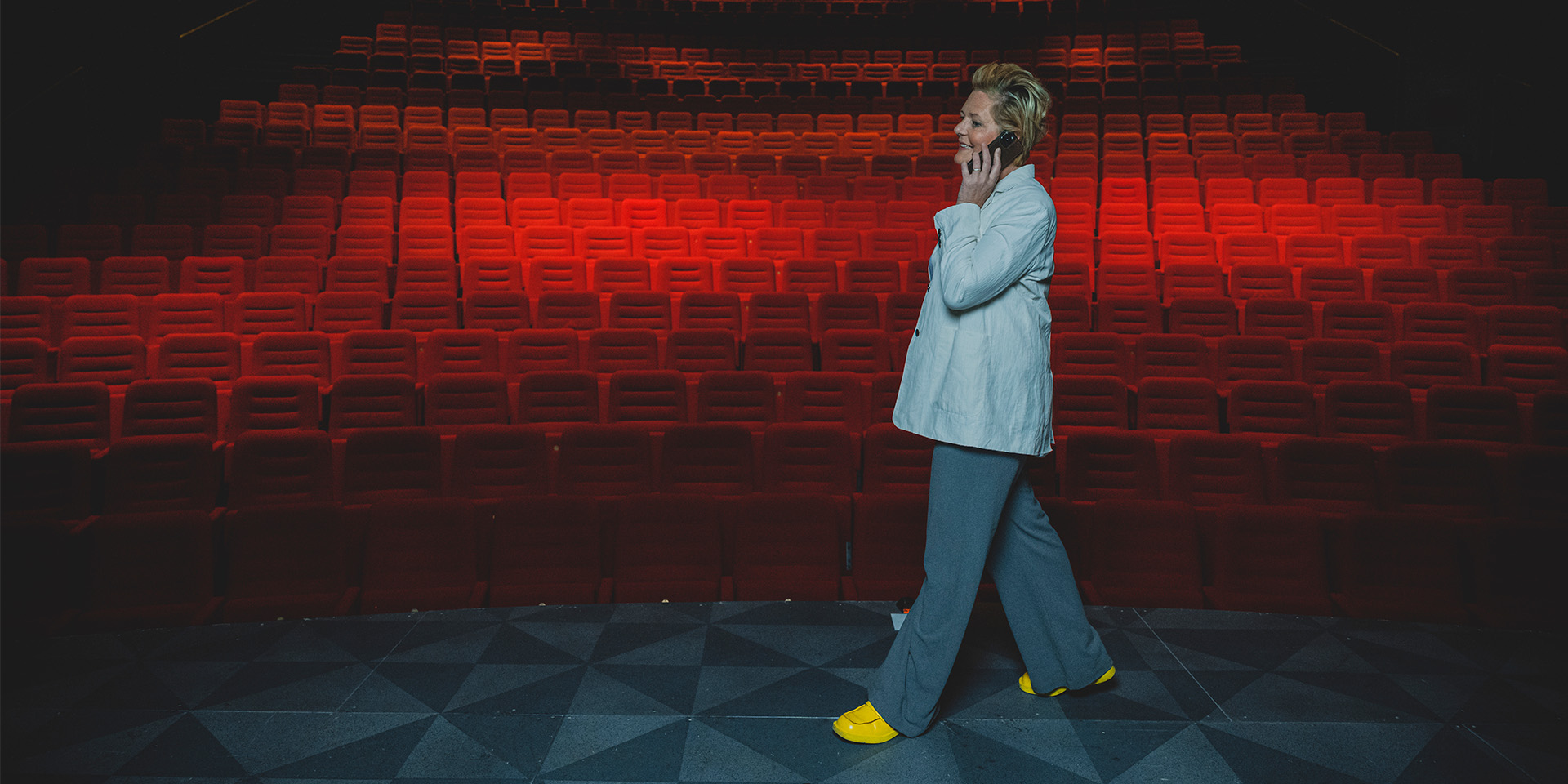 Mette Wolf går rundt på scenen med røde teatersæder i baggrunden