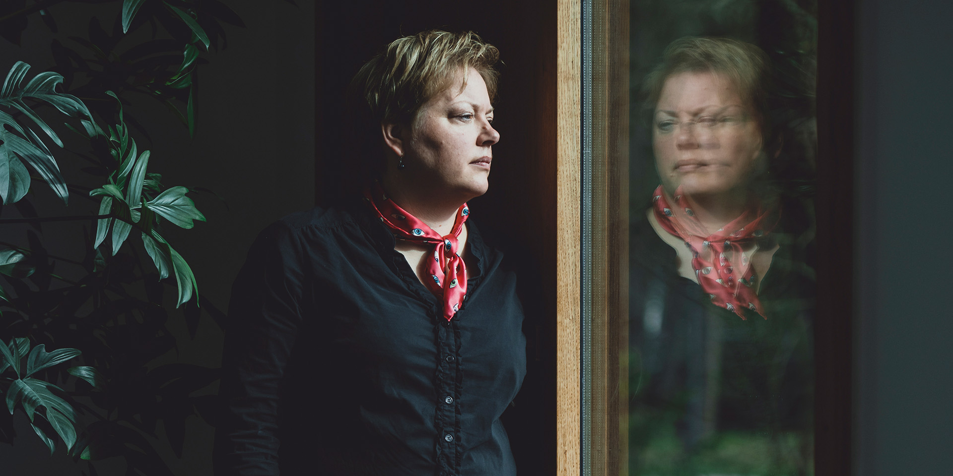 Nina Jørgensen står og ser ud af et vindue hvori man kan se hendes refleksion