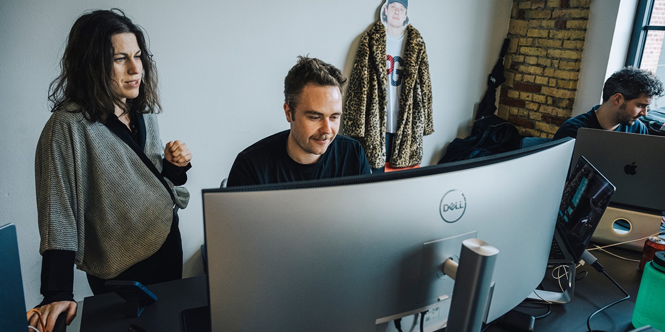 Sophie Bohr Grønbæk står og snakker med ung medarbejder ved skrivebord